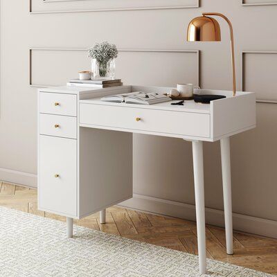 a white desk with two drawers and a gold lamp on the wall next to it