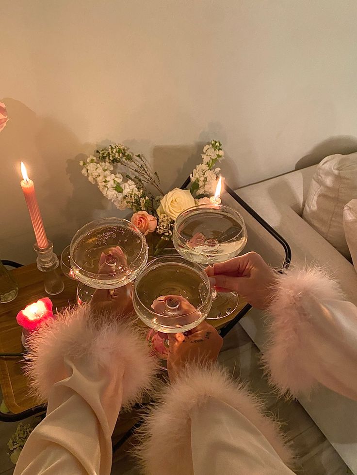 two people toasting with wine glasses in front of candles and flowers on a table