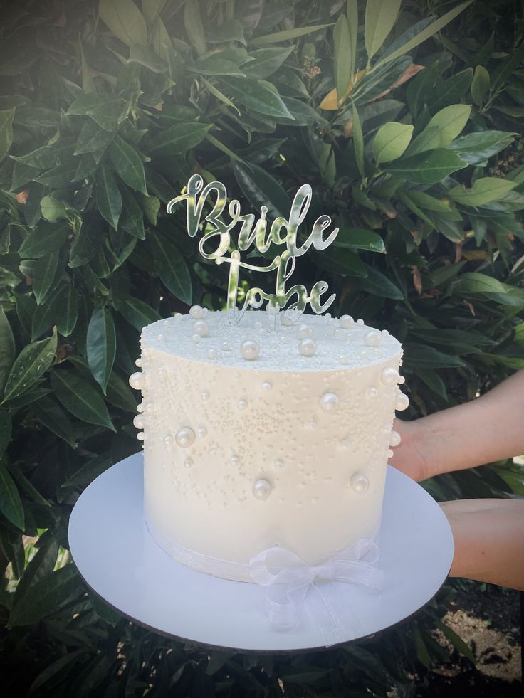 a white cake sitting on top of a blue plate next to a bush and green leaves