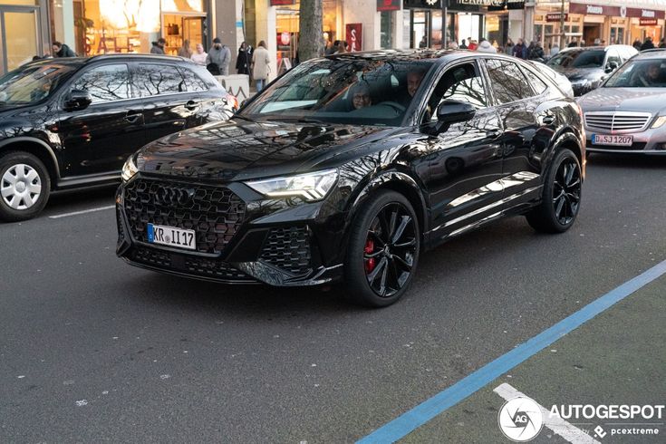 an audi suv is parked on the side of the road in front of other cars