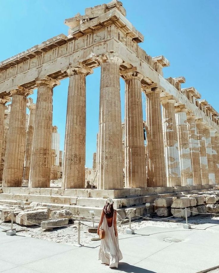 a woman standing in front of the ruins of an ancient building with columns and pillars