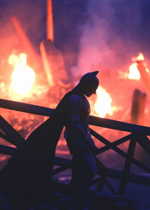 a man dressed as batman standing in front of a fire