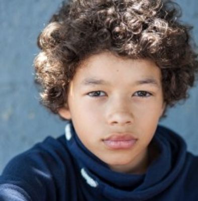 a young boy with curly hair is looking at the camera while wearing a blue shirt