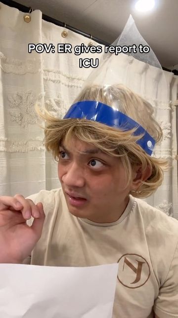 a young man wearing a plastic headband and holding a piece of paper in front of his face