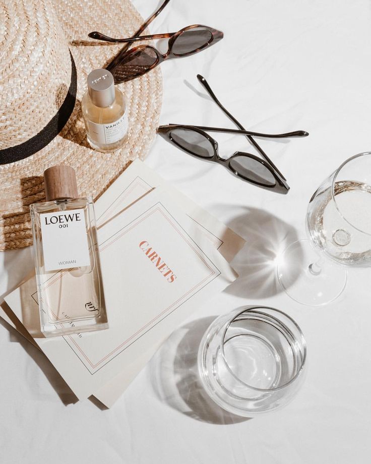 the contents of a hat, sunglasses, and perfume bottle are laid out on a table