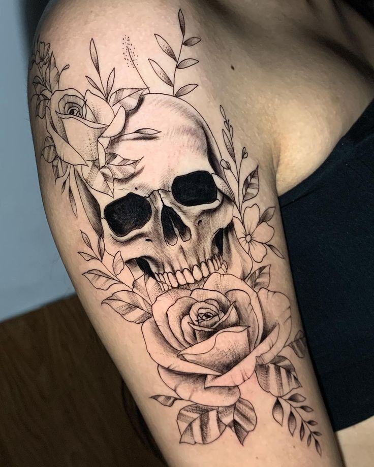 a woman with a skull and roses tattoo on her arm is holding a rose in front of her shoulder