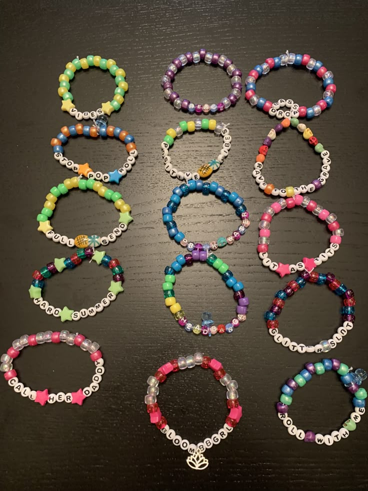 six bracelets with different colored beads and charms on a black surface, all lined up in the same row