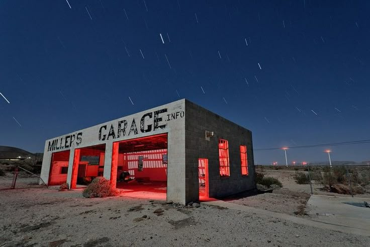 an old gas station with red lights on it's side and stars in the sky