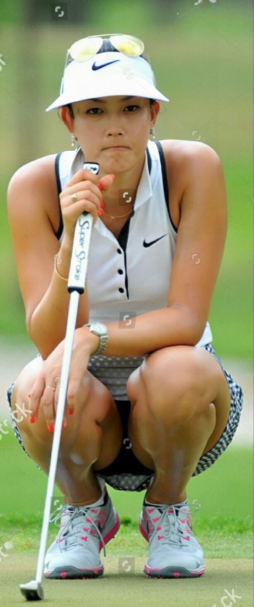 a woman kneeling down on the ground with a golf club in her hand and wearing a white hat