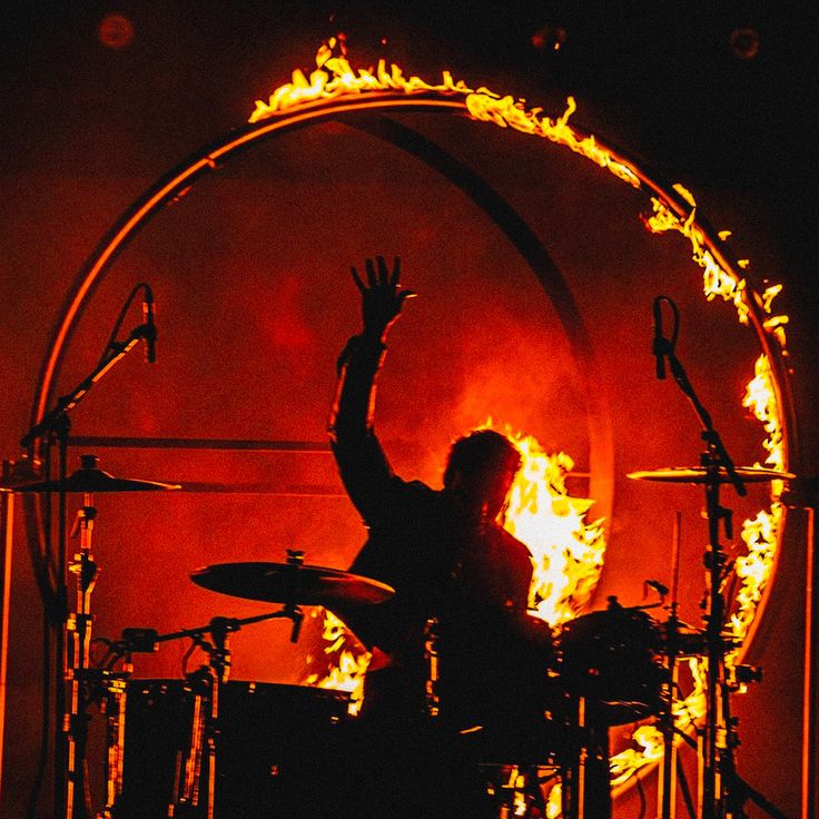 a man with his arms in the air behind a drum set on fire and flames