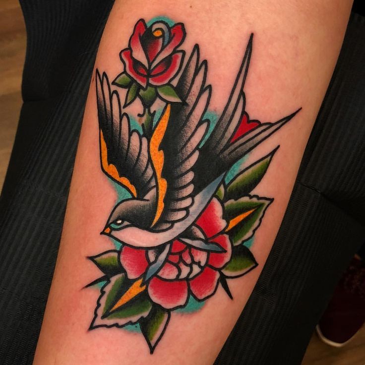 a bird with flowers on it's arm is sitting next to a rose tattoo