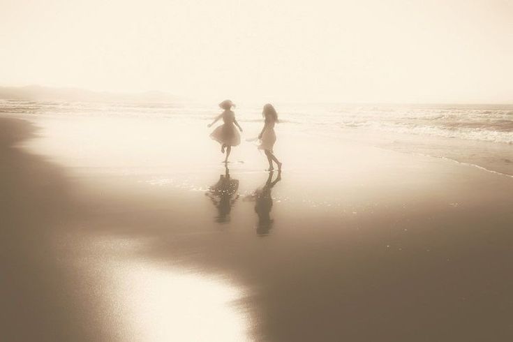 two girls are walking on the beach in front of the water at sunset or sunrise