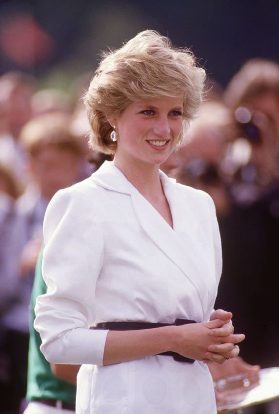 the princess of wales smiles as she stands in front of an audience wearing a white coat and black belt