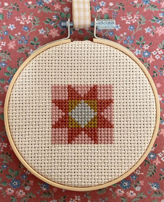 a cross stitch pattern with a flower in the center on a pink floral fabric background