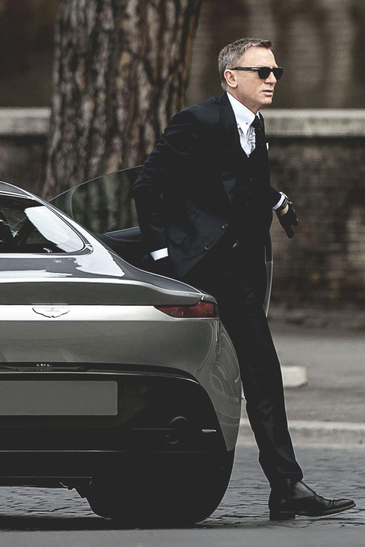 a man in a suit and sunglasses walking past a car