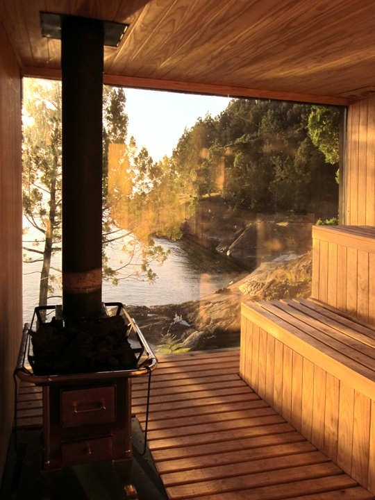 a wooden bench sitting next to a fire place on top of a wooden floor near a body of water