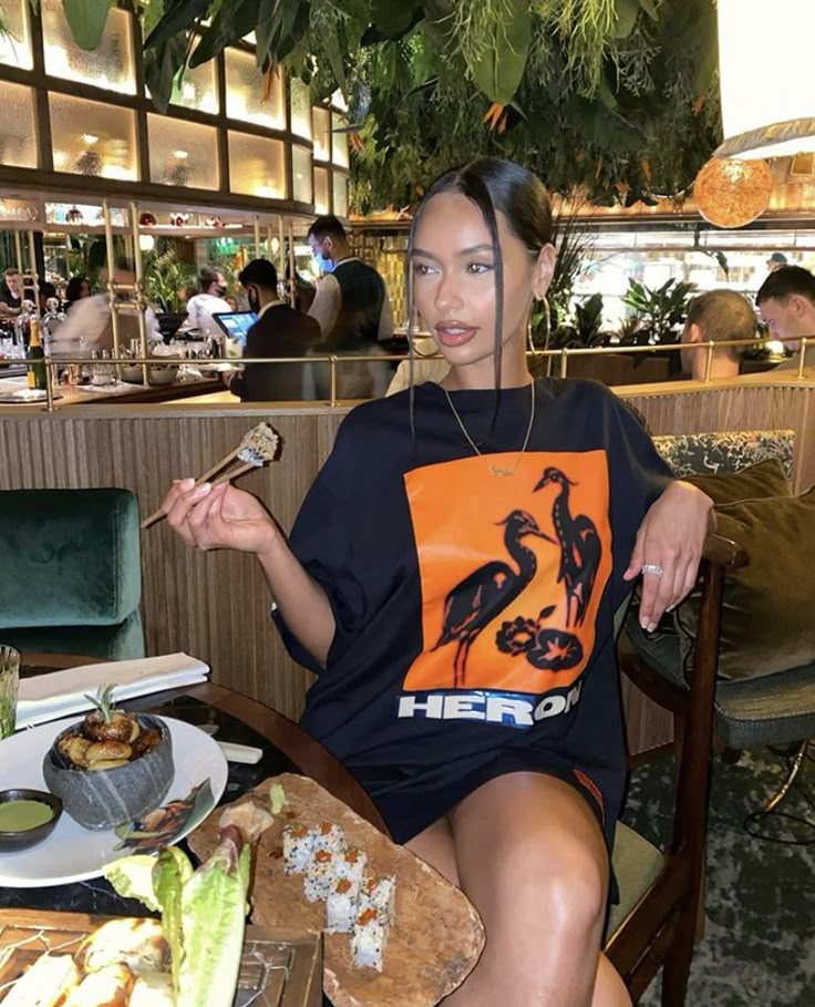 a woman sitting at a table with food in front of her and holding chopsticks