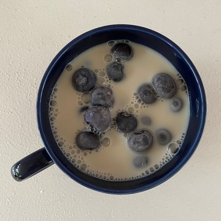 a cup filled with milk and blueberries on top of a white table next to a wall