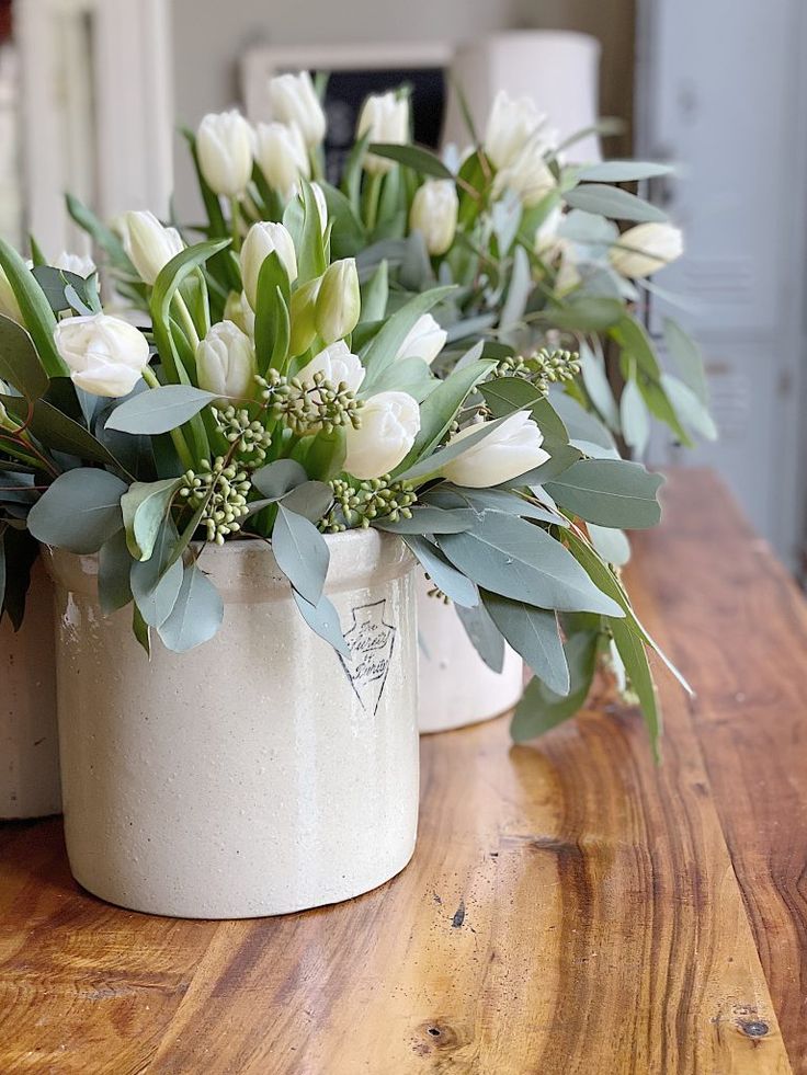 two white vases filled with flowers on top of a wooden table