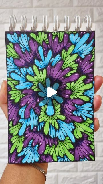 a hand holding up a spiral notebook with blue and green flowers on it