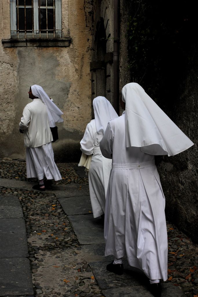 three women dressed in white are walking down the street with their backs turned to the camera