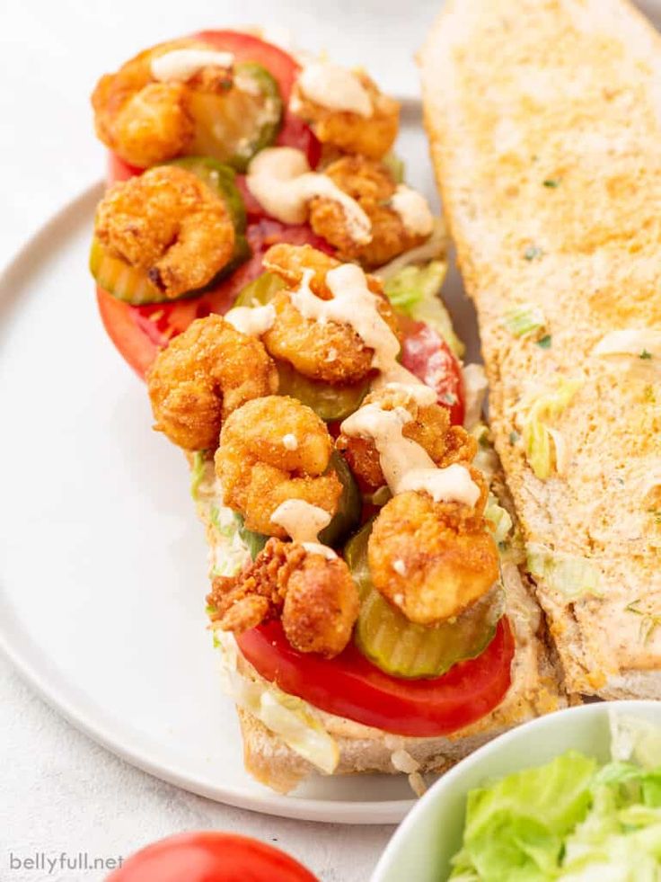 there is a sandwich with shrimp on it next to a bowl of lettuce and tomatoes