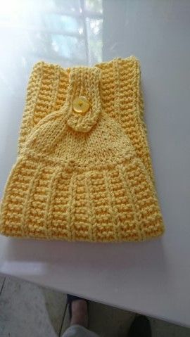 a crocheted yellow purse sitting on top of a white table next to a person's feet