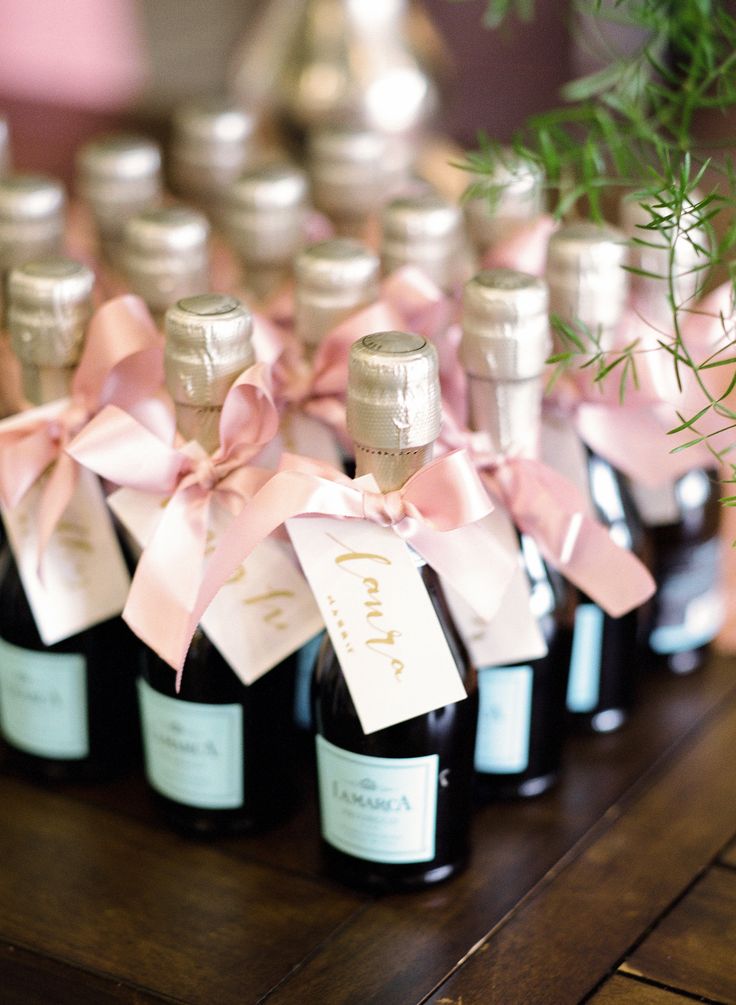 several bottles of wine with pink bows and labels on them sitting on a wooden table