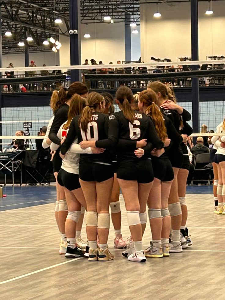 a group of girls huddle together in a circle on the court for a volleyball game