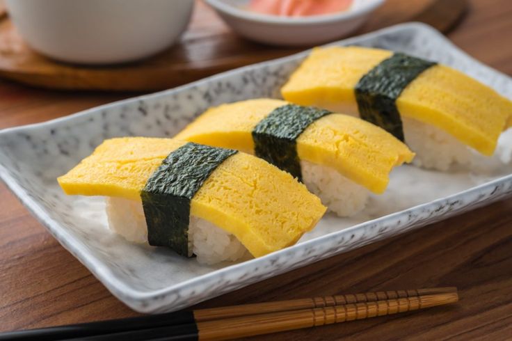 three pieces of sushi on a plate with chopsticks