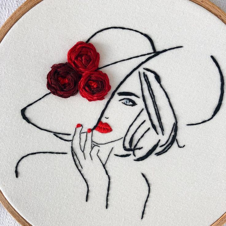 a woman's face with red roses on her hat is embroidered onto a white wall hanging