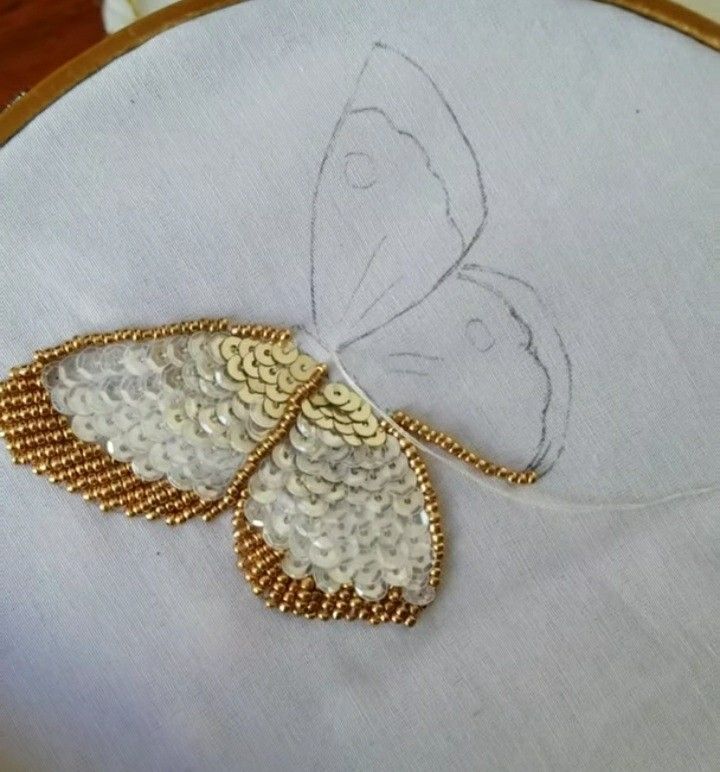 an embroidered butterfly on a white cloth with gold beading and thread in the hoop