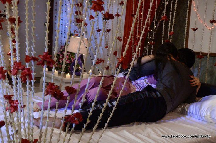 two people are laying on a bed with red and white flowers hanging from the ceiling