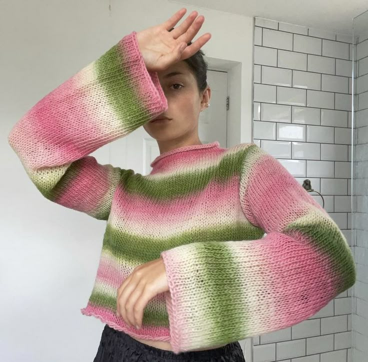 a woman wearing a pink, green and white sweater in front of a bathroom mirror