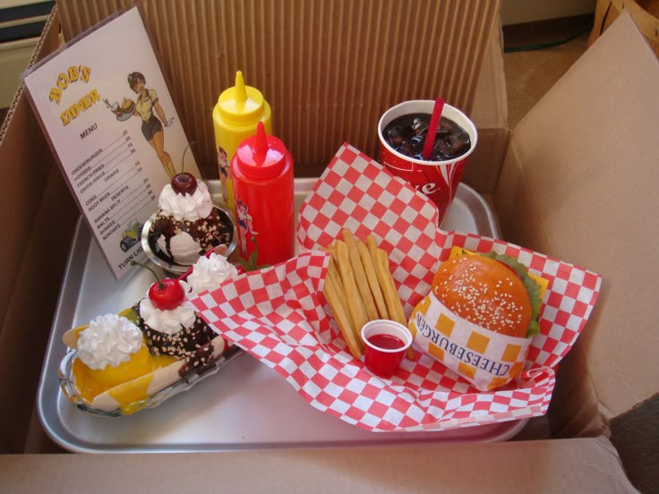 an open box with some food and drinks on the tray, including fries, hotdogs, ketchup