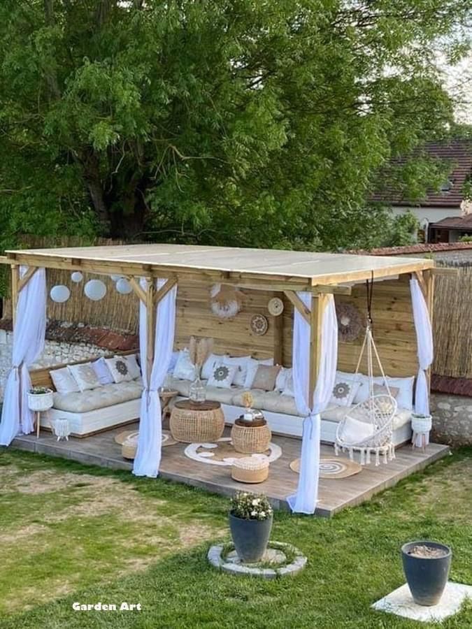 a wooden gazebo with white curtains and pillows on it