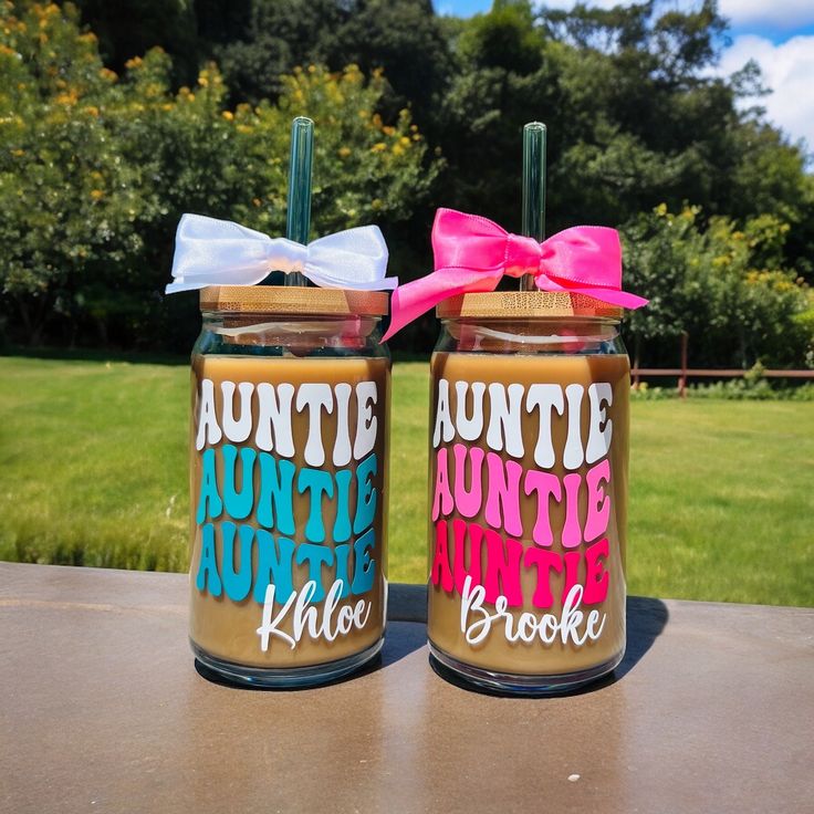 two mason jars with pink and blue bows are sitting on a table in front of some grass