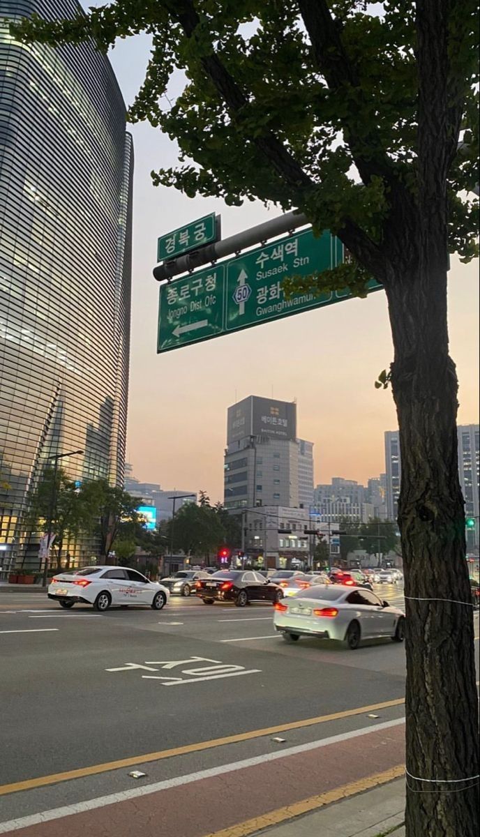 cars are driving down the street in front of tall buildings and skyscrapers at dusk