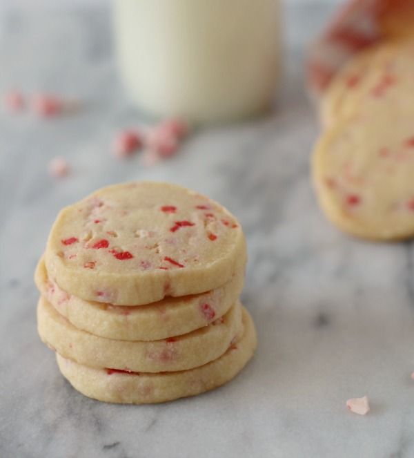 a stack of cookies next to a glass of milk on a marble counter top with pink and white sprinkles