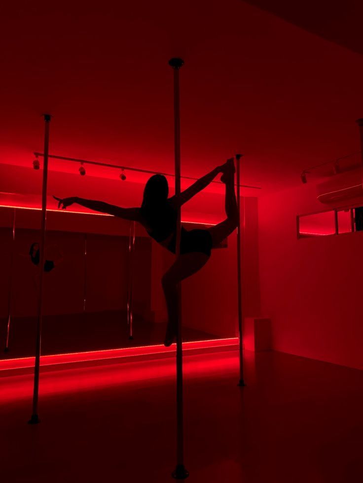 a woman standing on poles in the middle of a room with red lights behind her