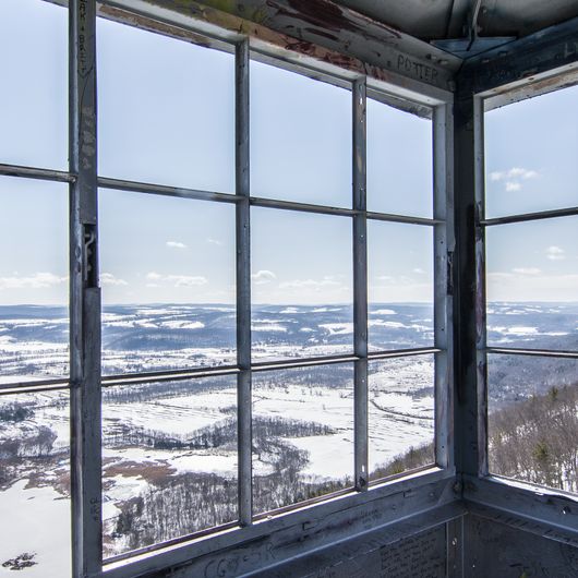 an open window in the side of a building with snow on the ground and trees outside