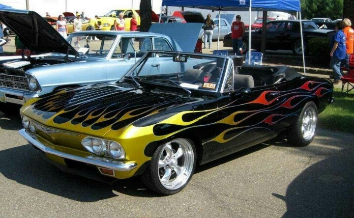 a yellow and black car with flames on it's hood parked next to other cars