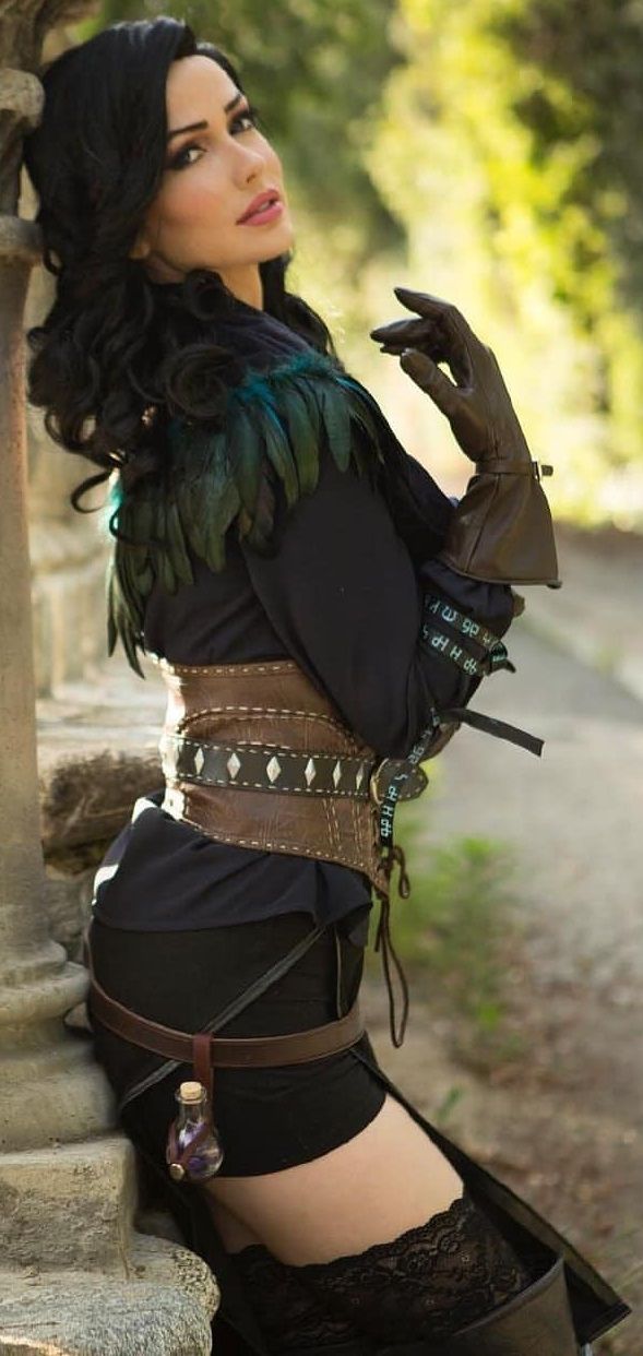 a woman with black hair and green feathers on her chest is leaning against a pillar