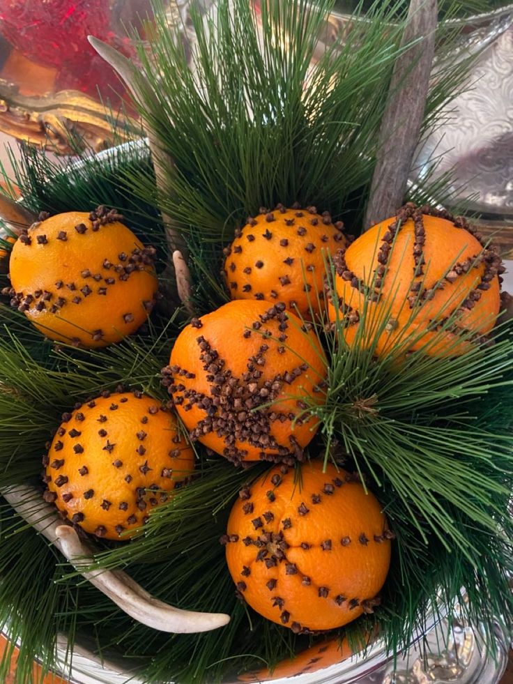 a bowl filled with oranges sitting on top of a table next to pine cones