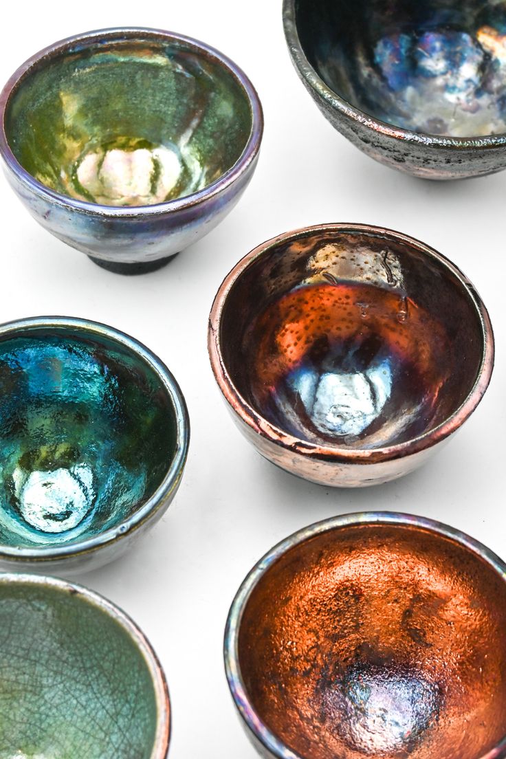 six bowls are lined up on a white surface, each with different colored glazes