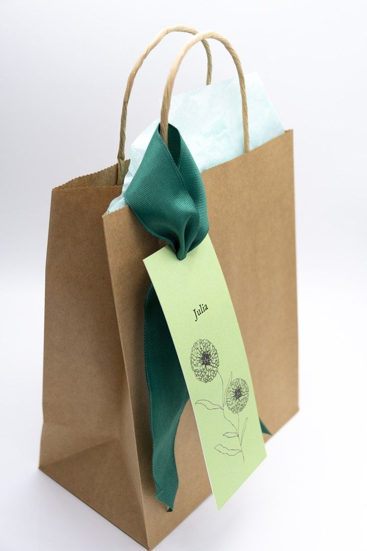 a brown paper bag with a green ribbon tied around it and a note attached to the handle