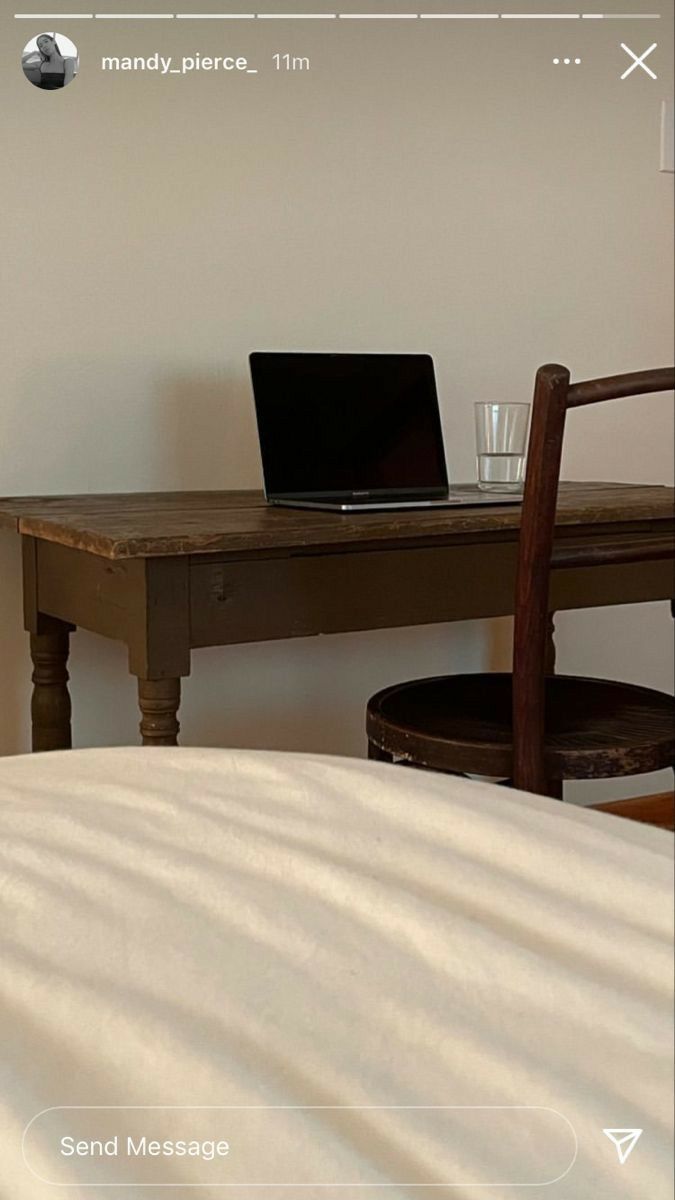 an open laptop computer sitting on top of a wooden desk next to a white bed