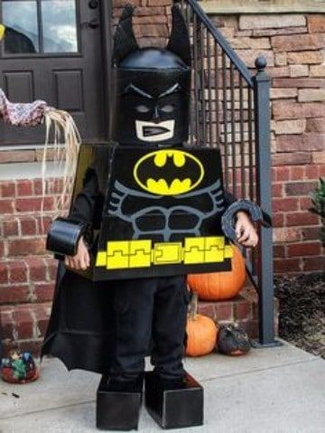 a little boy dressed up as batman standing in front of a house with pumpkins