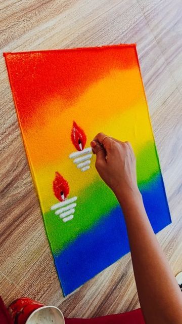 a person is painting on a canvas with candles and rainbow colors in the background, while another hand holds a paintbrush