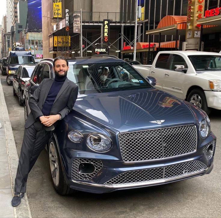 a man leaning on the hood of a car in front of parked cars and buildings